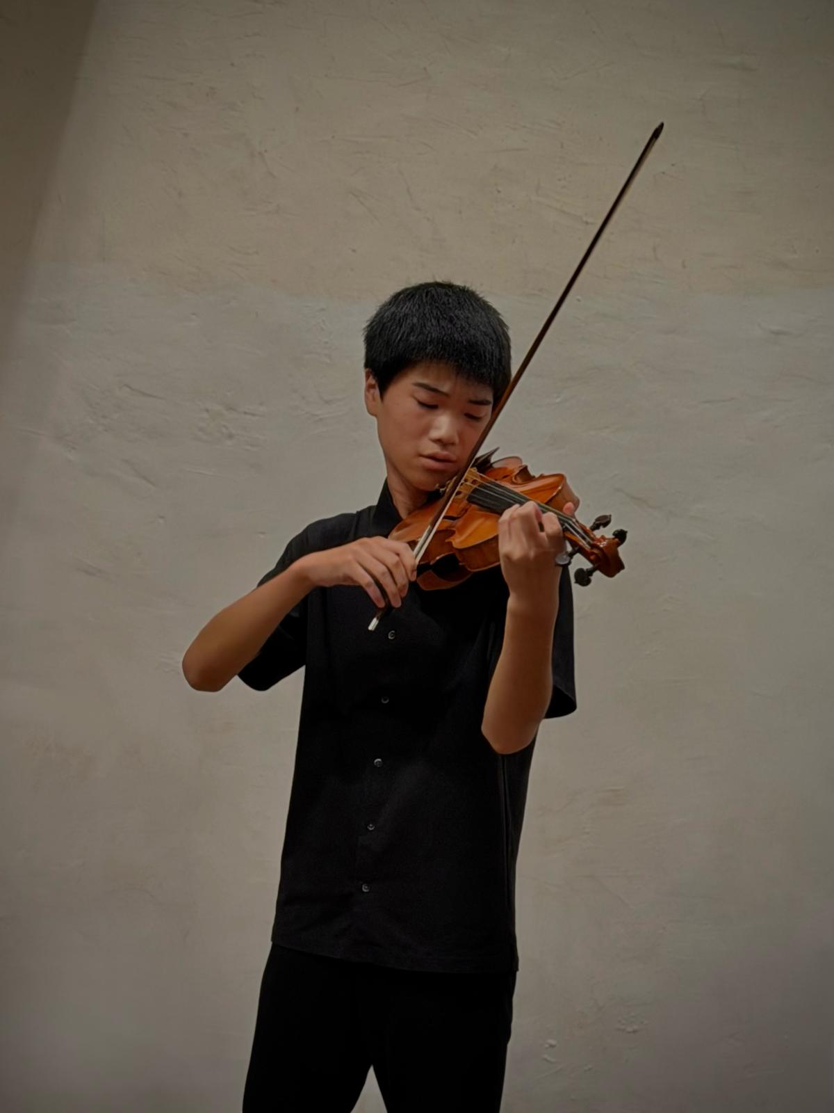Un jeune violoniste joue seul devant un mur clair