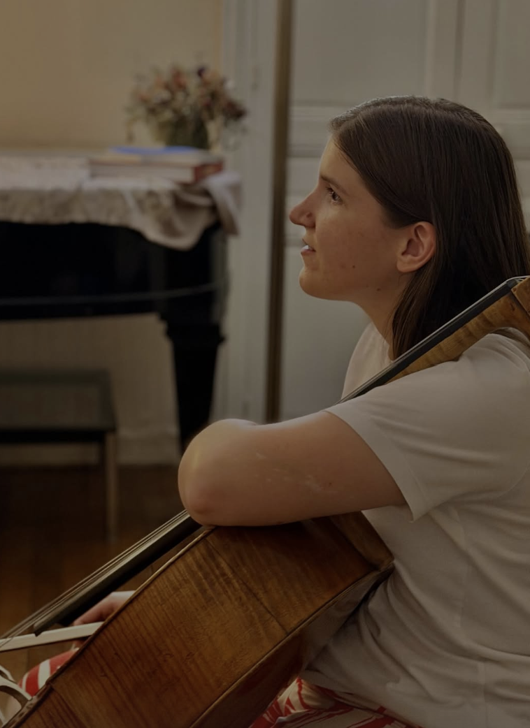 Une violoncelliste écoute, son instrument contre l’épaule, dans le salon